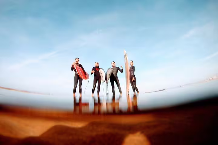 Group of surfers in wetsuits holding boards at Caparica beach, perfect for beginners and adventure seekers in Portugal.