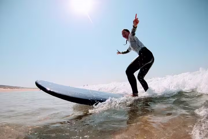 Surfer enjoying a thrilling ride on the waves at Caparica Surf Experience under a clear blue sky, perfect for adventure seekers.