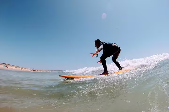Surfer riding a wave at Caparica Beach under clear blue skies, highlighting the exhilarating Caparica Surf Experience.
