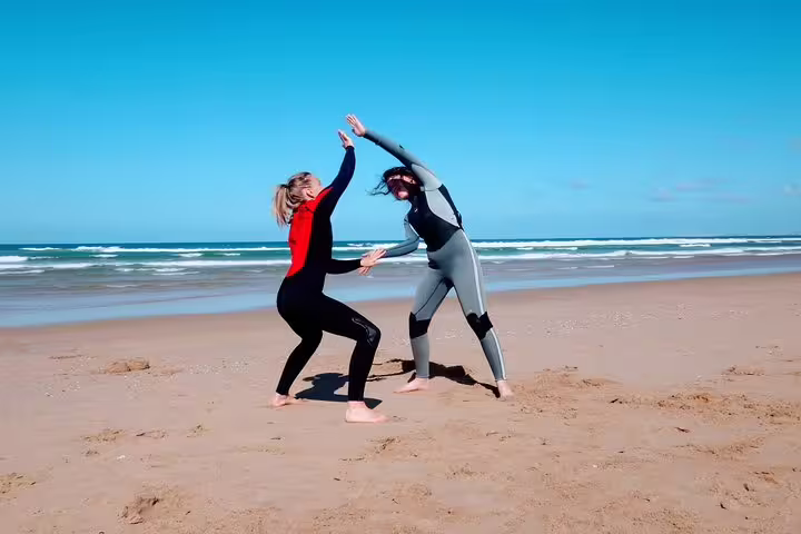 Two women in wetsuits practicing surf moves on Caparica Beach, highlighting the dynamic and engaging surf lessons experience.