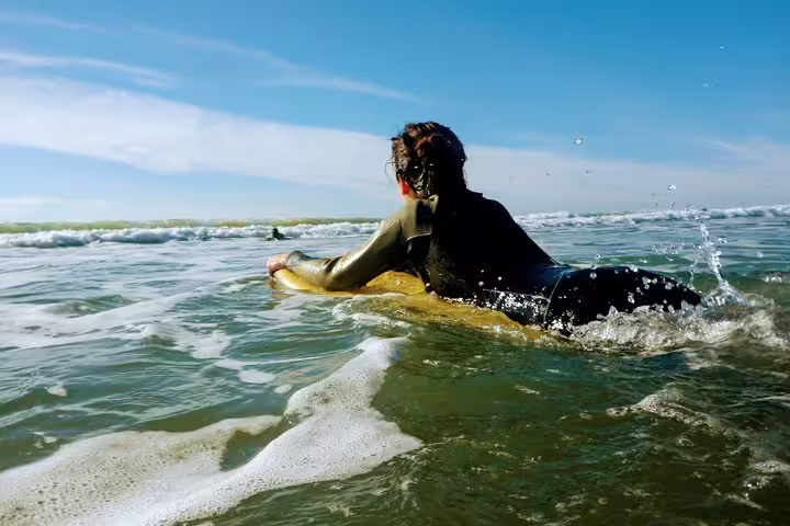 Surfer in wetsuit paddling on a surfboard in the vibrant ocean at Caparica, perfect for a surf and yoga retreat adventure.