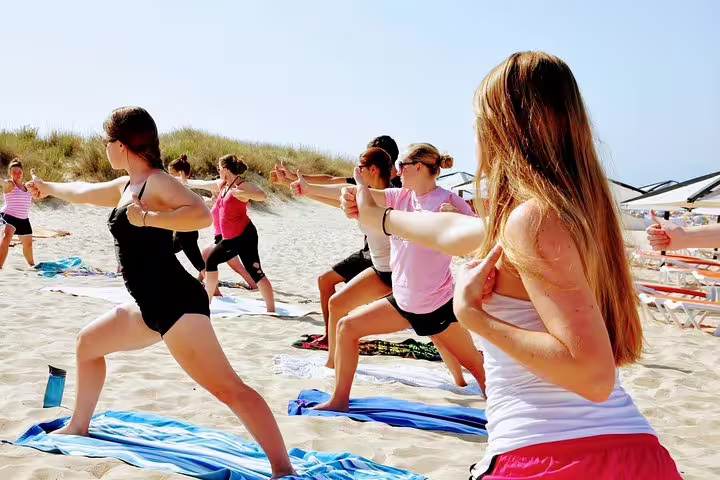 Participants practicing yoga on a sunny beach at Caparica, Portugal, during a surf and yoga retreat for relaxation and wellness.