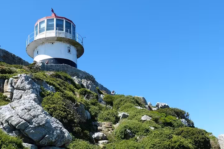 Lighthouse perched on a rocky, green hillside under a clear blue sky at Cape of Good Hope, Cape Town tour highlight.