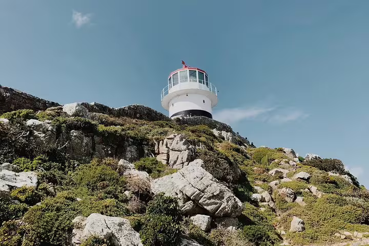 Iconic lighthouse perched on rocky hillside at Cape of Good Hope under a clear blue sky, a must-see on Cape Town tours.