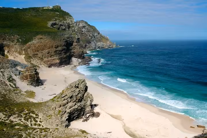 Scenic view of Cape Point's rugged cliffs and pristine beach meeting the turquoise ocean in Cape Town, South Africa.