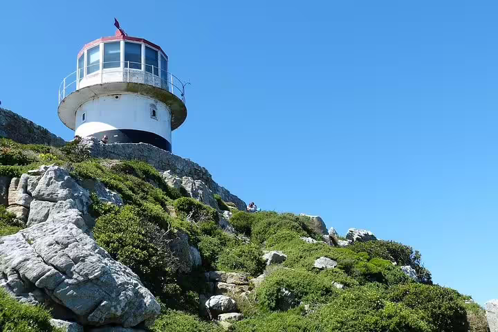 Historic lighthouse atop lush green hills under a clear blue sky at Cape Point, a highlight of the private day tour.