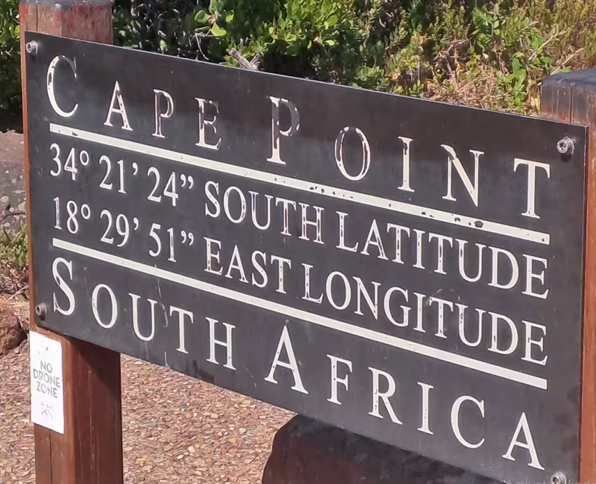 Cape Point sign displaying coordinates and location in South Africa, surrounded by greenery and no drone zone notice.