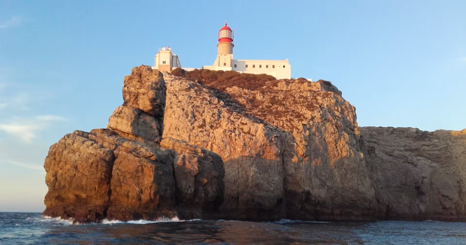 Sunset view of Cape St. Vincent lighthouse perched on rugged cliffs overlooking the Atlantic Ocean.