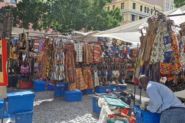 Bustling Cape Town market with vibrant African prints and crafts, a must-visit on a shopping tour with a private chauffeur.