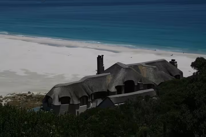 Scenic coastal view of a thatched-roof house overlooking a pristine beach on the Cape Town expedition.