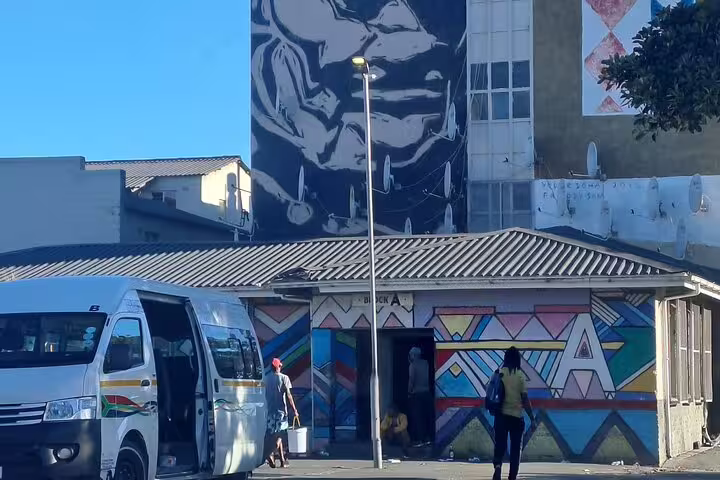 Street art and people near a taxi in Gugulethu, Cape Town, reflecting the lively culture and local transport.
