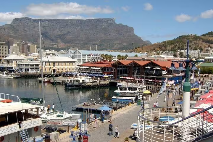 Bustling V&A Waterfront in Cape Town with boats docked and Table Mountain in the background under a clear sky.