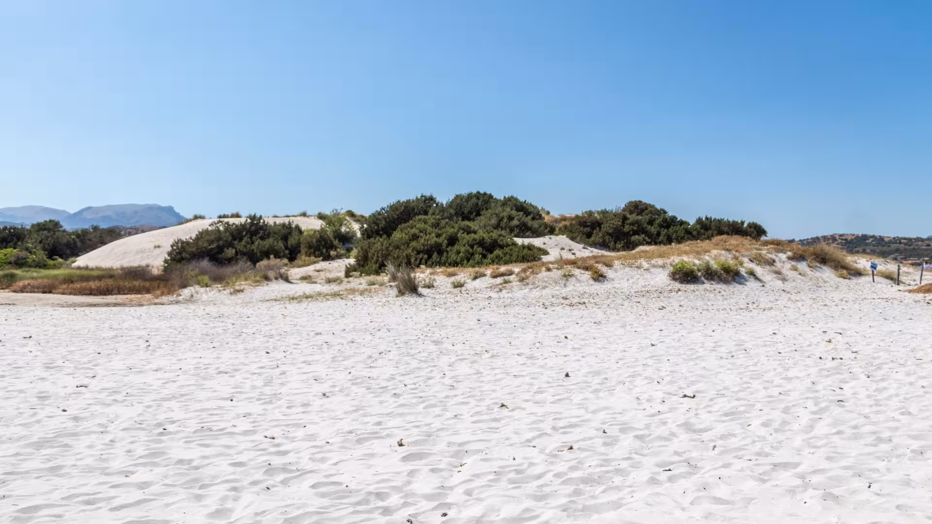 Pristine white sand dunes at Capo Comino beach under a clear blue sky, showcasing Sardinia's stunning coastal scenery.