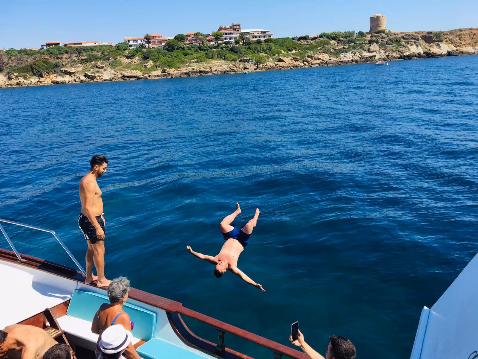 Tourists enjoy diving from a boat into the clear blue waters at Capo Rizzuto marine protected area, Italy.
