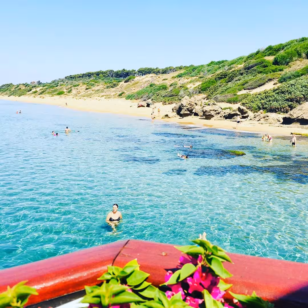 Serene beach scene with swimmers in crystal-clear waters at Capo Rizzuto marine protected area, Italy.