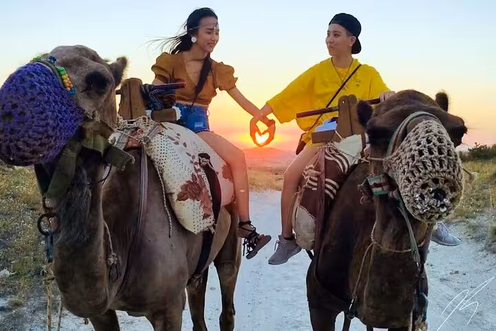 Couple on Cappadocia camel ride tour at sunset, holding hands on scenic valley trail in Turkey