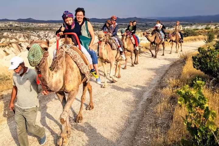Guided Cappadocia camel ride tour with travelers on a scenic valley trail near Göreme at sunset