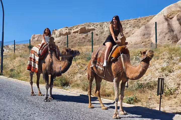 Travelers riding camels in Cappadocia landscape during 2-day Spanish tour with internal flights in Turkey