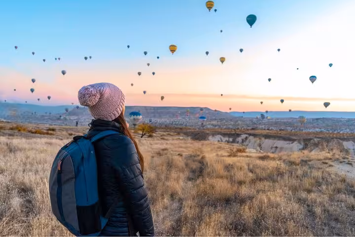 Traveler watches sunrise hot air balloons over Cappadocia valleys on full-day small group tour with lunch
