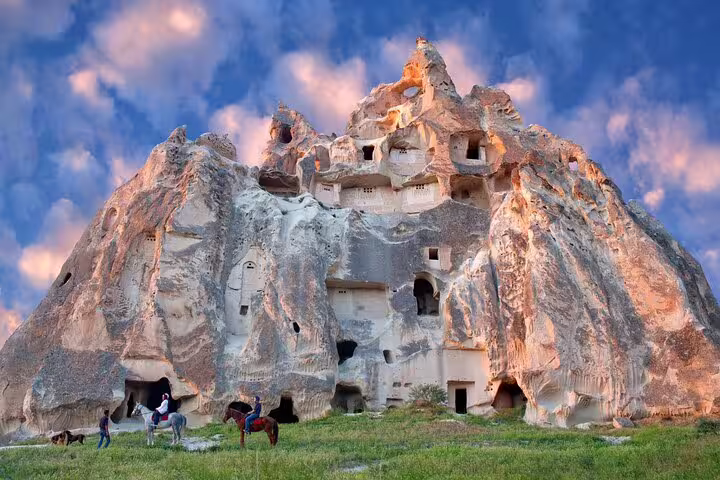 Discover Cappadocia's historic cave dwellings and rock formations with horseback riders beneath a vibrant sky on a private tour.