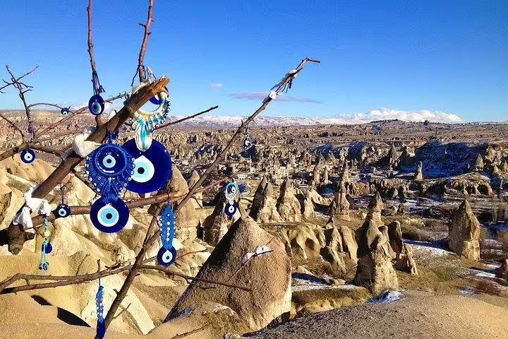 Evil eye charms hang on a tree with Cappadocia's stunning rock formations in the background, seen on a private tour.