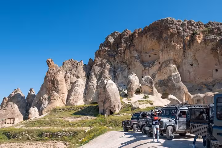 4x4 vehicles parked by Cappadocia cliffs and cave rooms near Uçhisar, part of the Cappadocia Red Tour