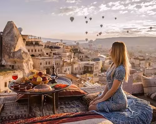 Traveler sitting on a terrace overlooking Cappadocia while hot air balloons lift at sunrise