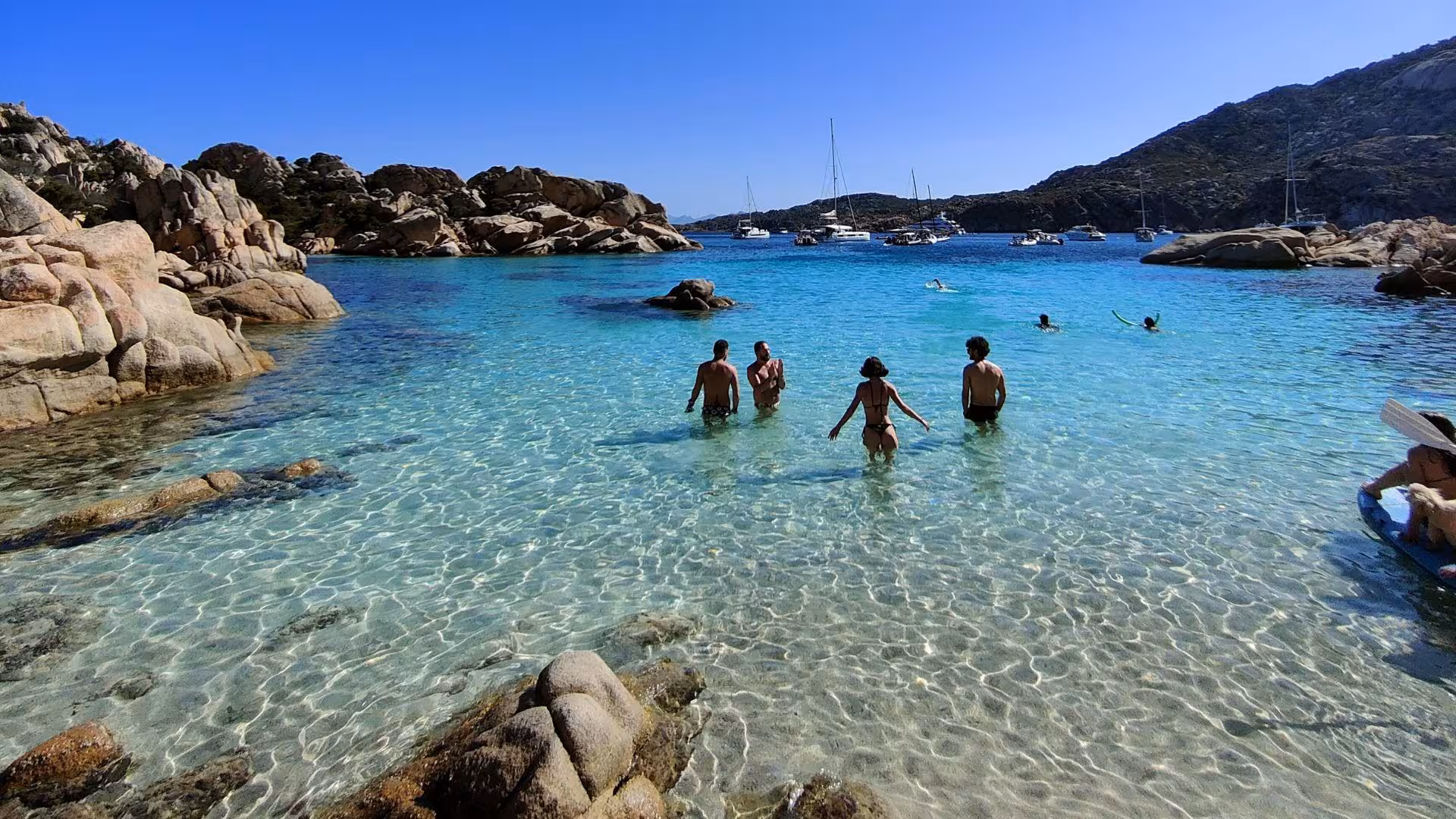 Visitors swim in crystal-clear waters at Cala Coticcio, a hidden gem on Caprera Island's scenic hiking route.