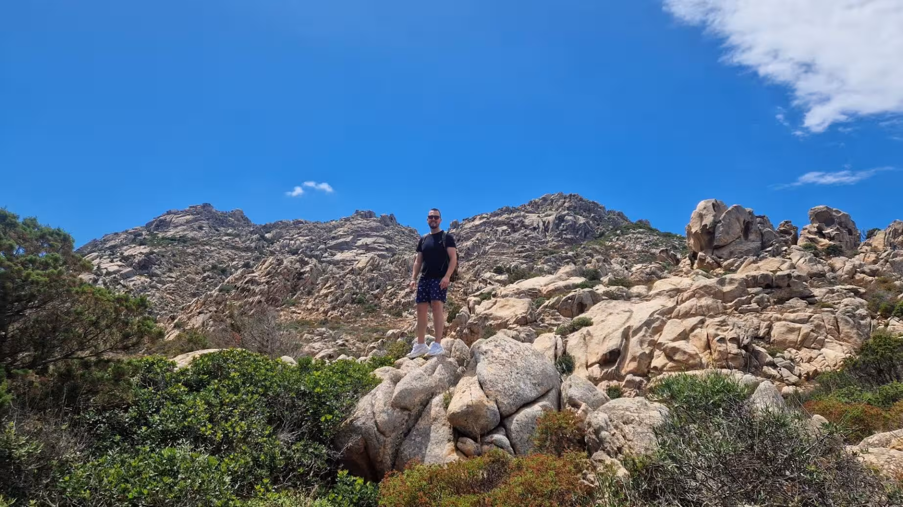 Hiker stands on rocky terrain under a clear blue sky on Caprera, showcasing the rugged beauty of the island hike.