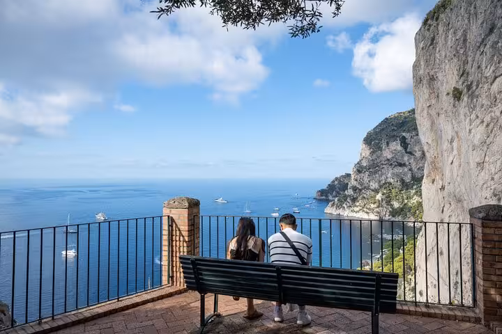 Couple enjoying a breathtaking view of the cliffs and sea from a bench in Capri, featured in the Blue Grotto visit tour.