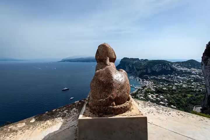 Stunning view of Capri's coastline and the Mediterranean Sea from a scenic overlook, featuring a stone statue.