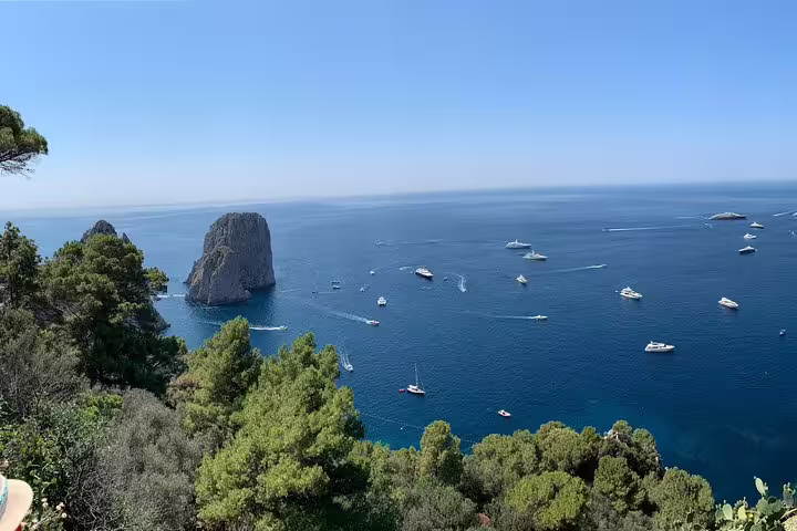 Breathtaking view of Capri's coastline with Faraglioni rocks and boats cruising the azure waters, ideal for sightseeing tours.