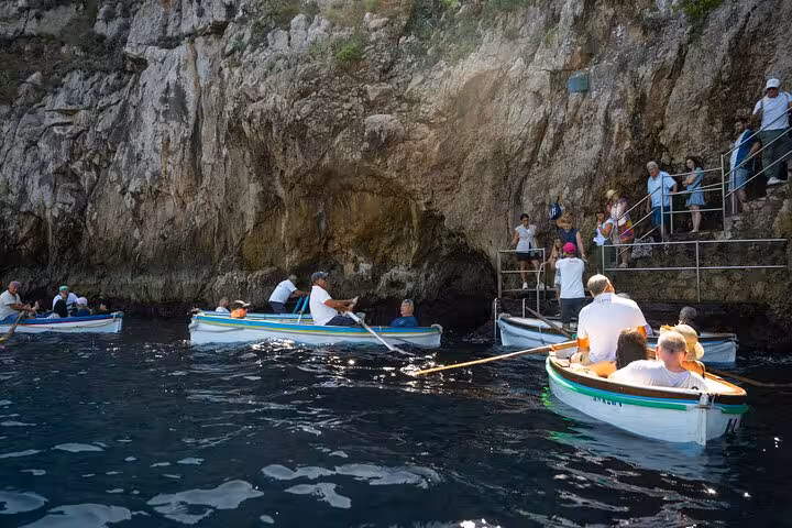 Tourists in rowboats exploring the entrance to the Blue Grotto on a sunny day during the Capri and Anacapri tour.