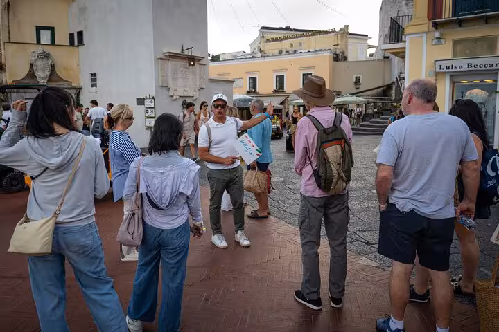 Group of tourists listening to a guide in a lively Capri square, highlighting the cultural aspect of the Blue Grotto tour.