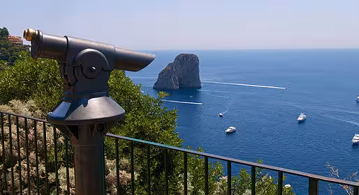 Scenic view of Capri's coastline with a telescope overlooking the Faraglioni rock formations and sailing boats.