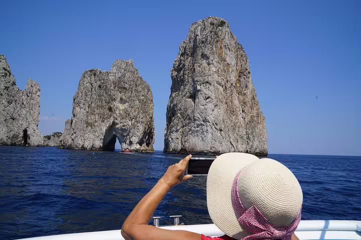 Tourist capturing the iconic Faraglioni rock formations from a boat on the Capri & Anacapri tour from Sorrento.