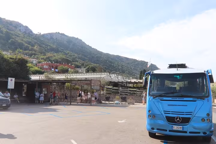 Blue tour bus at Anacapri ticket station with scenic mountain backdrop on Capri day tour.