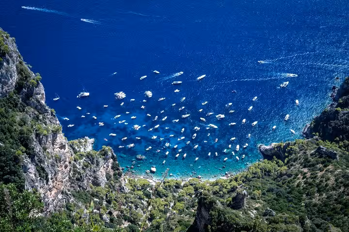 Aerial view of boats dotting the vibrant blue waters of Capri's coastline on a full-day island tour.
