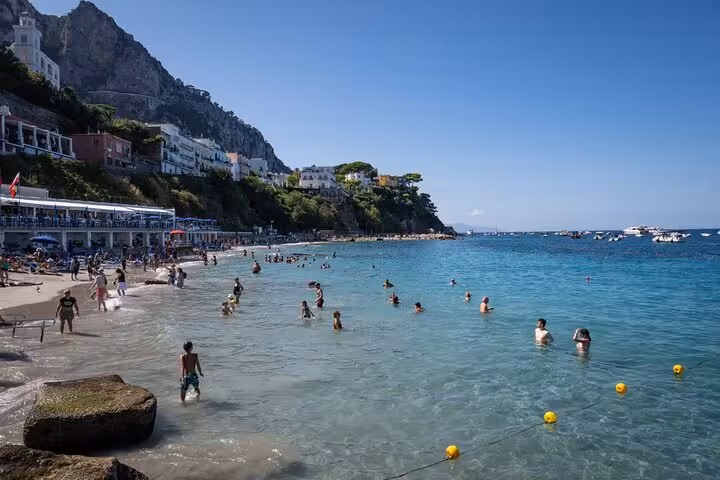 Tourists enjoying a swim in the clear blue waters of a beautiful Capri beach, surrounded by stunning cliffs.