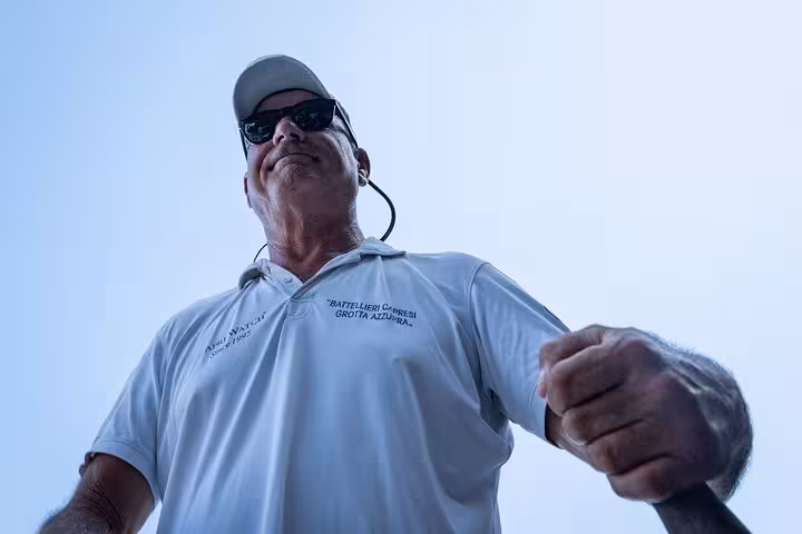 Tour guide in sunglasses and cap steering a boat in Capri, part of the Blue Grotto all-inclusive experience.