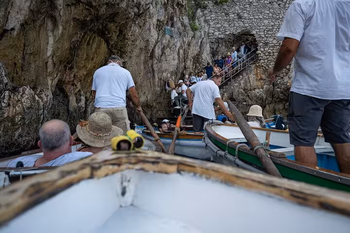 Tourists in small boats entering the Blue Grotto cave on a guided exploration tour of Capri's stunning coastline.