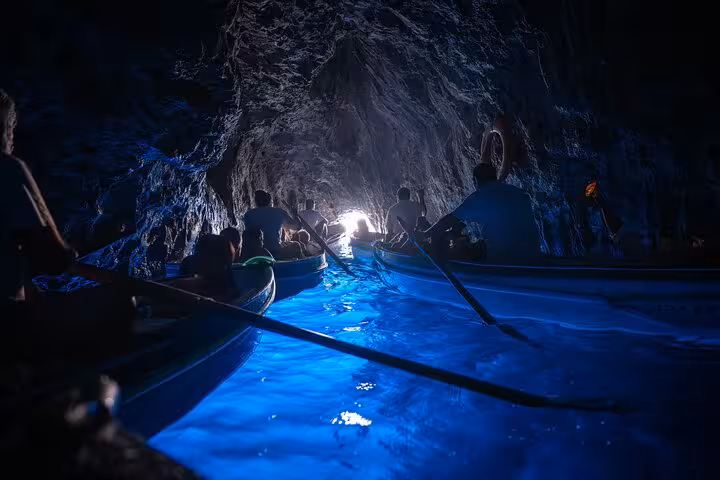 Boats filled with tourists navigate the enchanting Blue Grotto's glowing blue waters, a highlight of Capri tours.