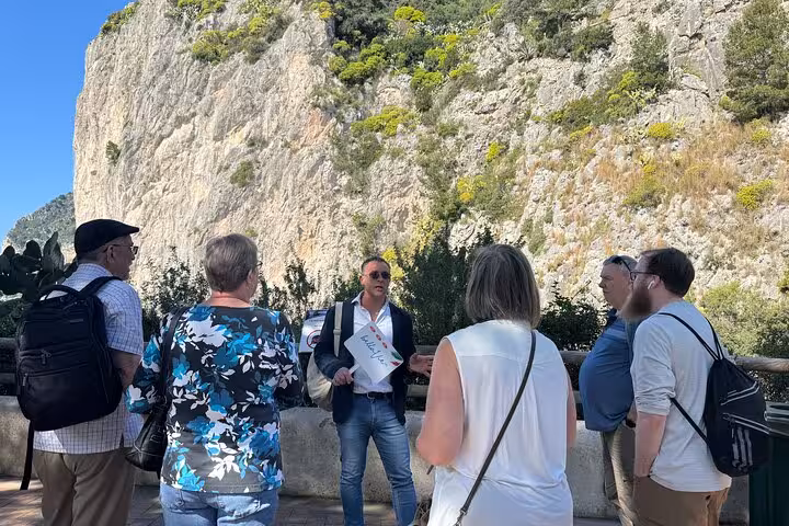 Tour guide leading a group near the scenic cliffs of Capri on a Blue Grotto and Faraglioni shore excursion.