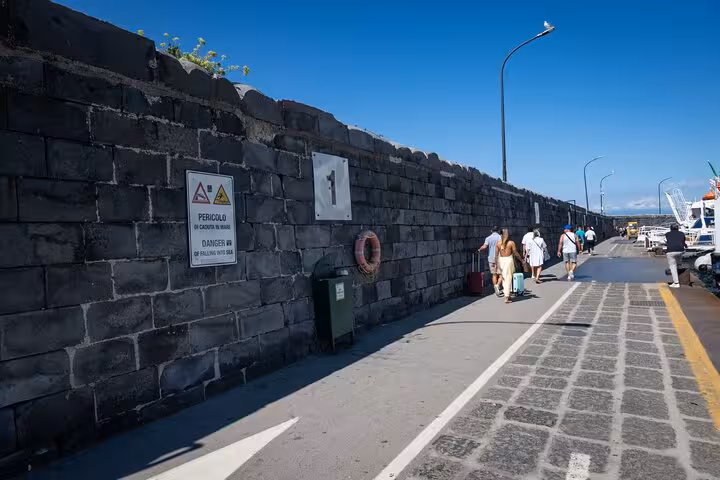 Visitors walking along a scenic harbor path on a sunny day during the Capri and Blue Grotto full-day tour.