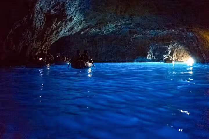 Full-day private boat tour to Capri Blue Grotto, glowing turquoise cave waters and small boats inside