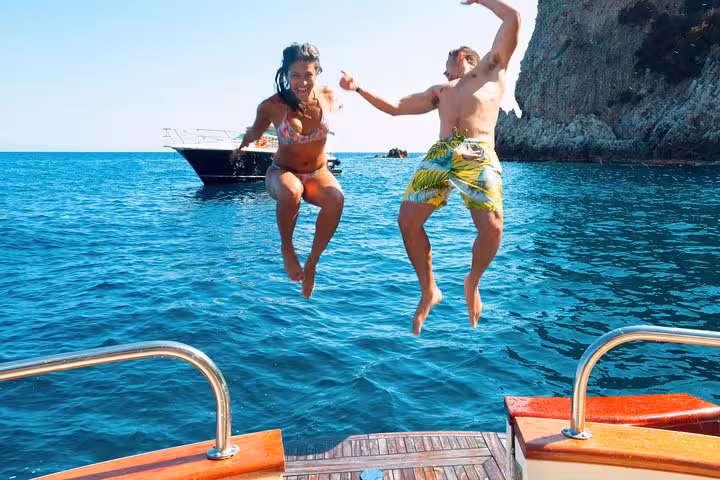 Two people joyfully jump into the clear blue waters of Capri during a vibrant small group tour from Sorrento.