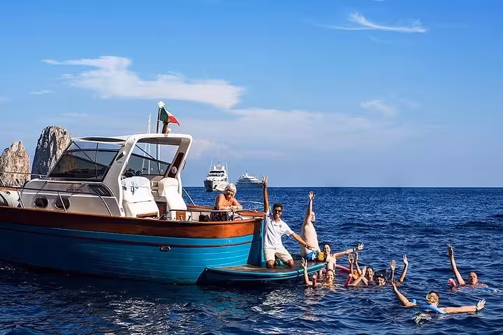 Tourists enjoy swimming and relaxing beside a boat in the azure waters around Capri on a Sorrento day trip.