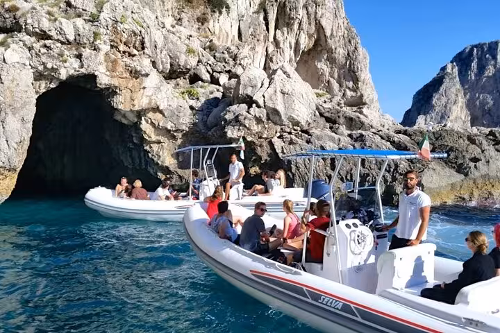 Tourists exploring the Blue Grotto in Capri on inflatable boats, part of a Sorrento day trip.