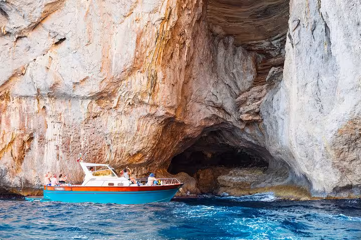 Small boat exploring majestic sea cave formations along Capri coastline on Amalfi excursion.