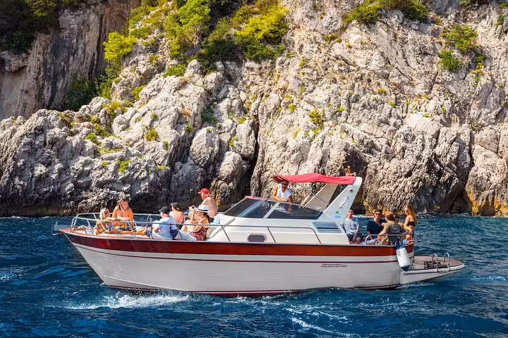 Tourists enjoy a very small group boat tour along the rugged coast of Capri, showcasing crystal-clear blue waters.